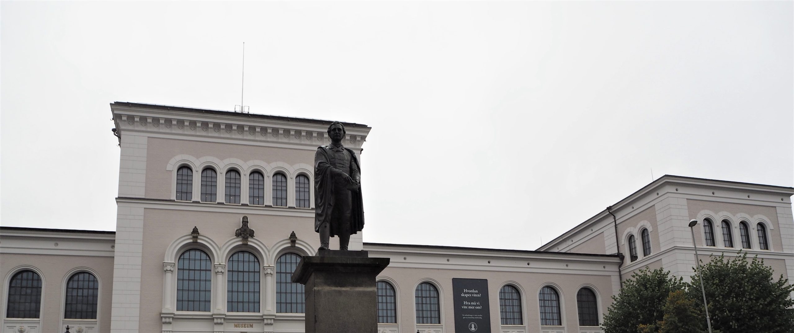 Statue av mannsperson, Christie, framfor eit stort, lyst bygg, Bergen Museum.
